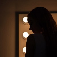 Силуэт девушки на фоне лампочек по краям большого зеркала