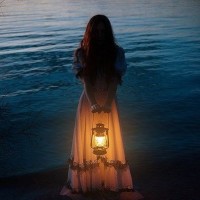 Девушка в платье стоит у воды с фонарём в руках