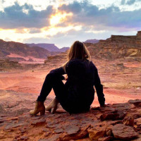 Девушка сидит в пустыне и смотрит на красивое небо
