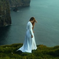 Девушка в длинном белом платье стоит у обрыва