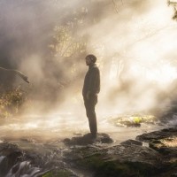 Мужчина стоит перед водопадом на фоне тумана