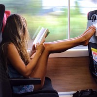Девушка читает книгу, упершись ногами в сиденье пассажира спереди
