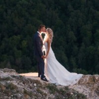 Свадебное фото с поцелуем на вершине горы на фоне леса