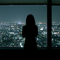 Силуэт девушки, стоящей у окна, на фоне ночного города.