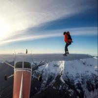 Человек стоит на крыле самолёта, летящего высоко над горами