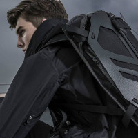 Сидящий мужчина в чёрной куртке с крутым рюкзаком на спине