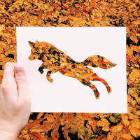 Силуэт лисы, вырезанный в листе бумаги на фоне осенних листьев