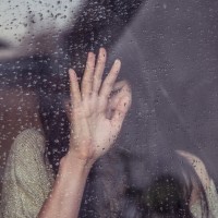 Девушка с тёмными волосами за окном покрытым дождевыми каплями.