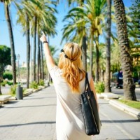 Стоящая спиной девушка указывает пальцем на пальмы вдоль дороги