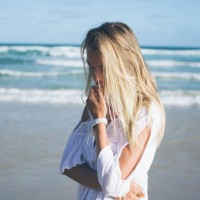 Блондинка в белой одежде с рукой у лица на фоне моря