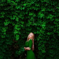 Девушка в зелёном платье на фоне стены обросшей вьющимся растением