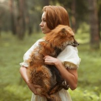 Рыжая девушка держит лису на руках на фоне леса